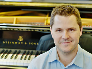 Julien Bret Portrait de Julien Bret avec un piano à queue Steinway & Sons à l’arrière-plan